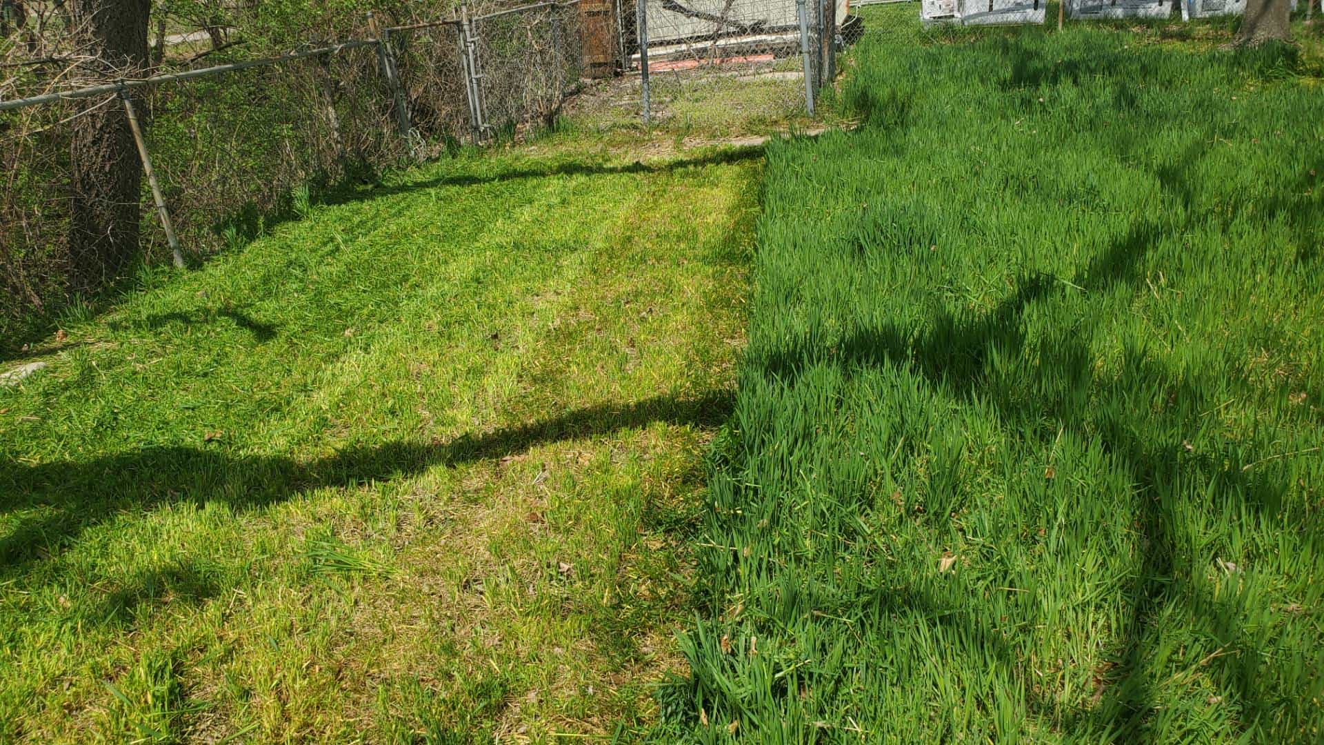 Close-up of muddy commercial lawn mowers on a grassy field under cloudy skies, showing wear from recent mowing on wet terrain.