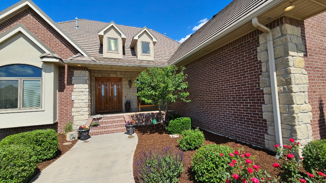 Brick home with landscaped front yard featuring fresh mulch, trimmed bushes, flowering plants, and a small tree near the entryway.