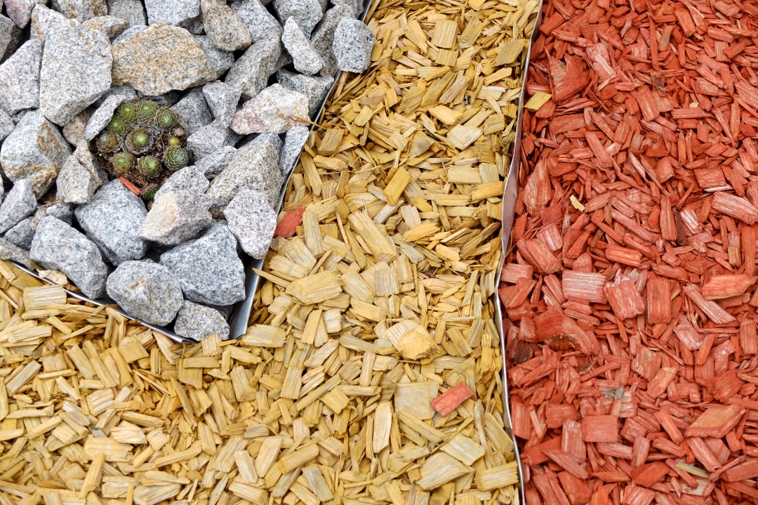 Landscape materials showing gray gravel, natural wood mulch, and red mulch separated by metal edging for outdoor landscaping