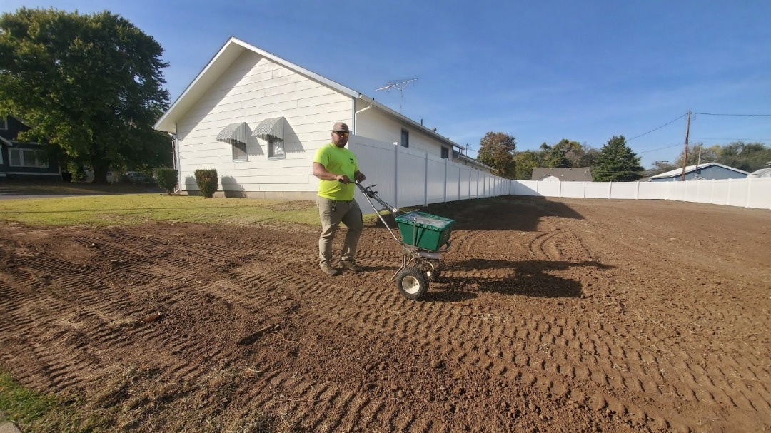 Lawn care expert using a spreader to seed and prepare soil for new grass growth in a residential backyard.